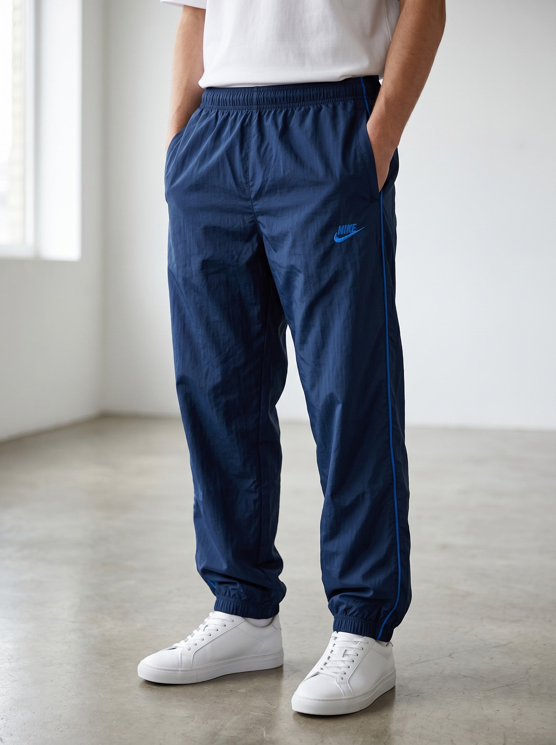 Nike navy blue nylon track pants with a light sheen and contrasting blue side stripes. Size S.